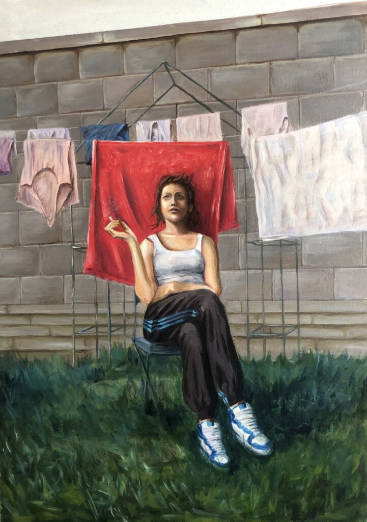 Oil painting of a young woman in tracksuit pants and sneakers, sitting in front of a red towel hanging on a drying rack. Surrounding her are pieces of underwear and laundry against a grey wall. Holding a cigarette, she stares ahead with a calm, distant gaze. The scene evokes themes of modern femininity, survival, and dignity in mundane settings.